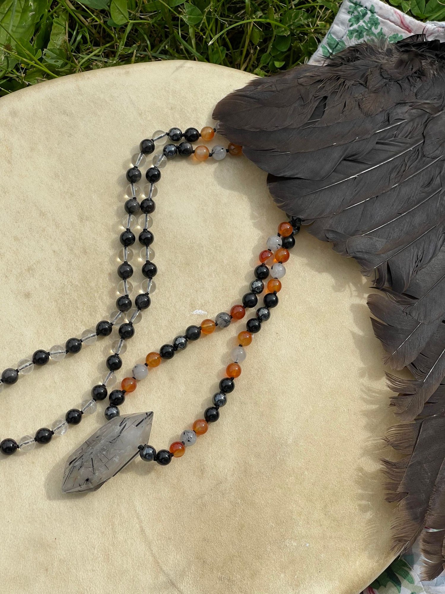 Tourmaline in Quartz, Hematite, Obsidian, Carnelian, & Clear Quartz Ceremonial Adorment, laying on a hide drum next to a crow wing